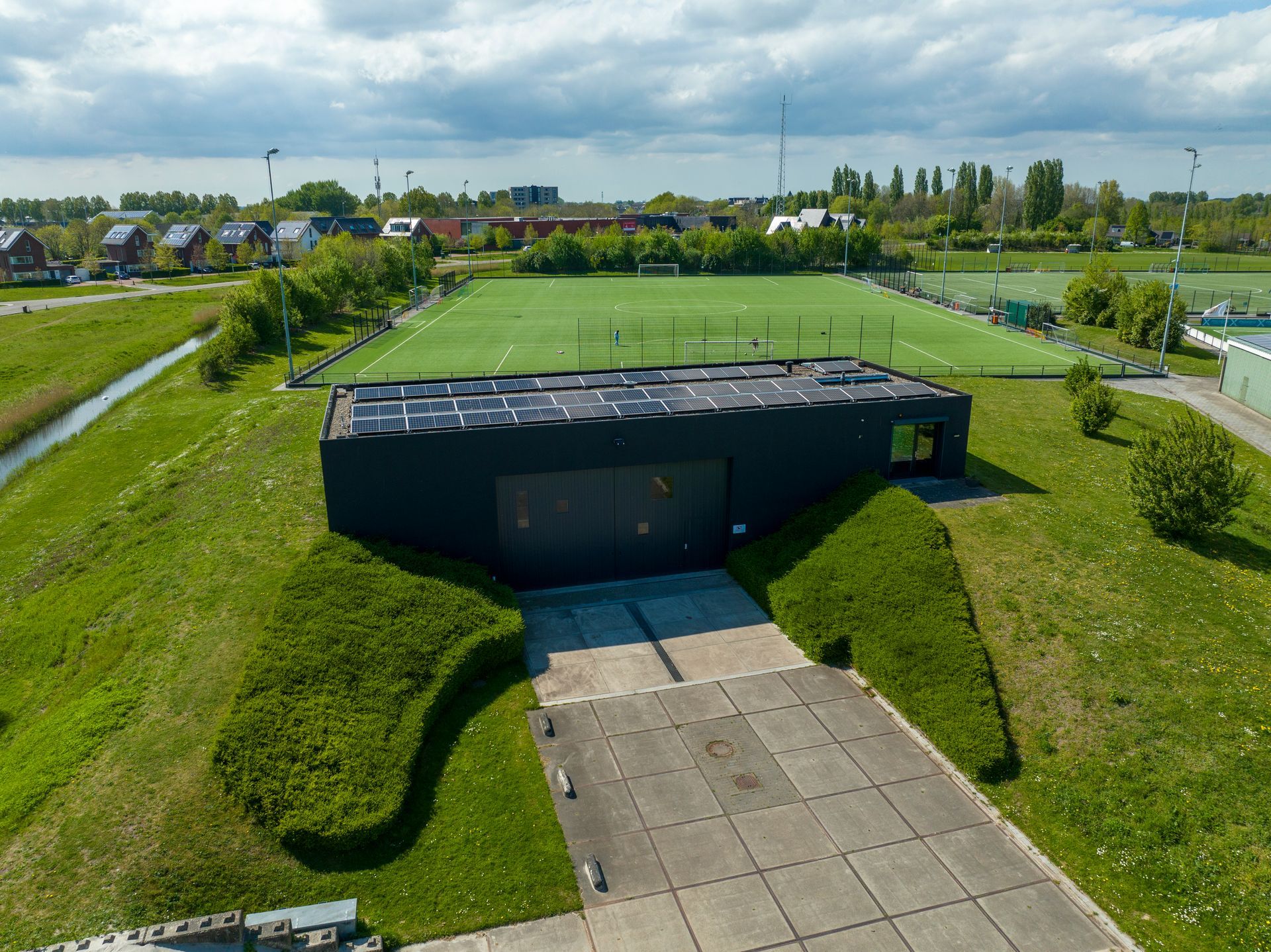 Een luchtfoto van een voetbalveld en een gebouw met zonnepanelen op het dak.