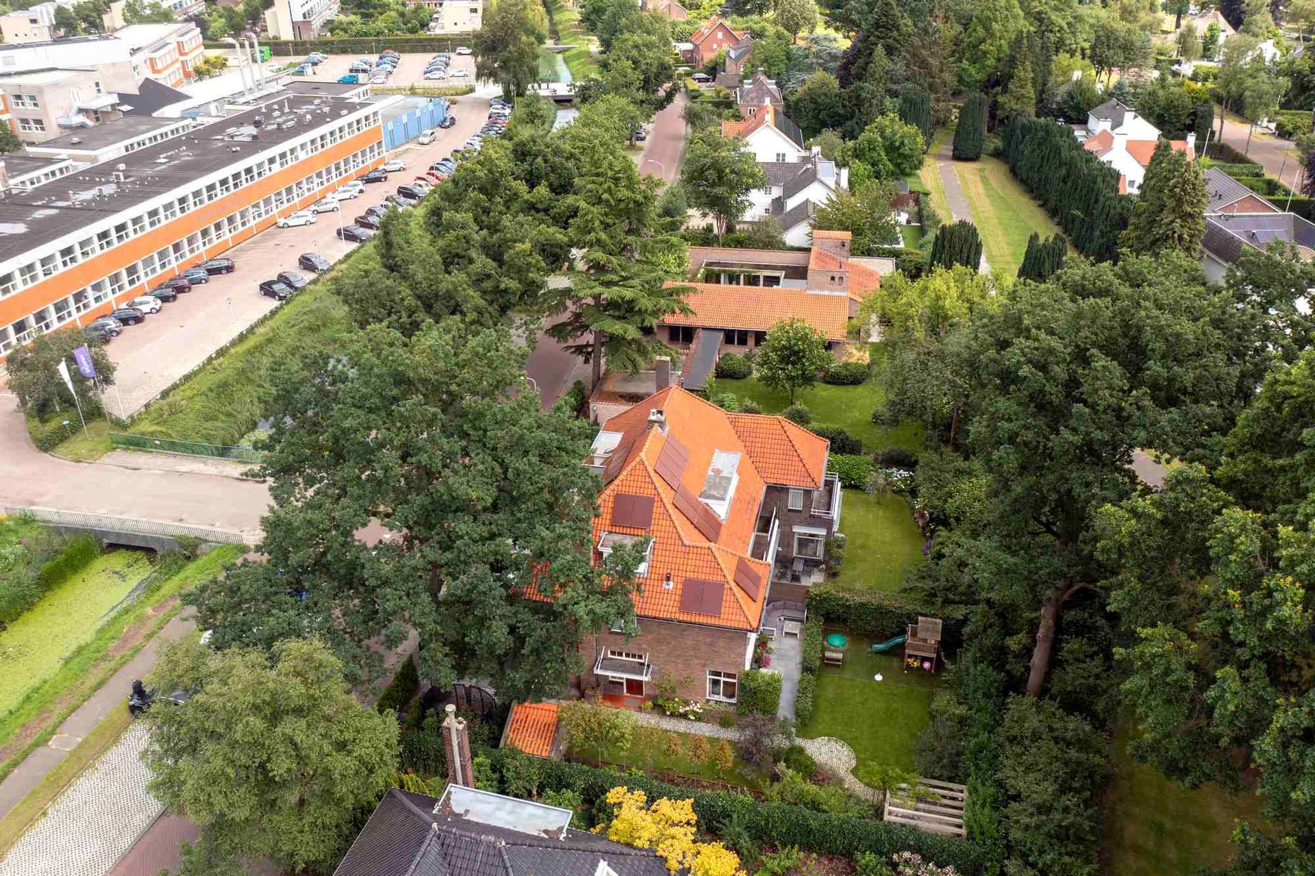 Een luchtfoto van een huis met een rood dak in een woonwijk, omgeven door bomen.