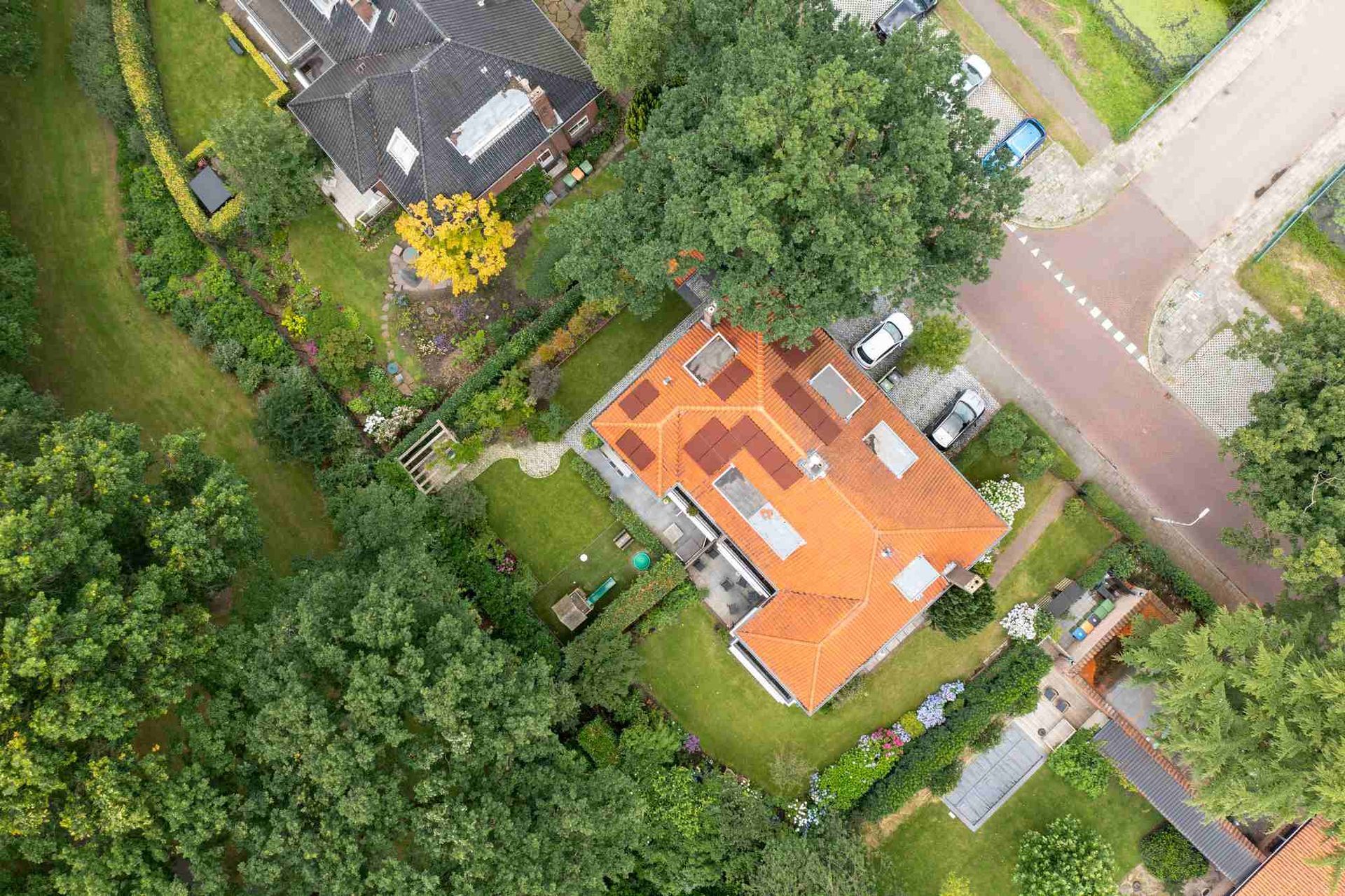 Een luchtfoto van een huis met een rood dak in een woonwijk, omgeven door bomen.