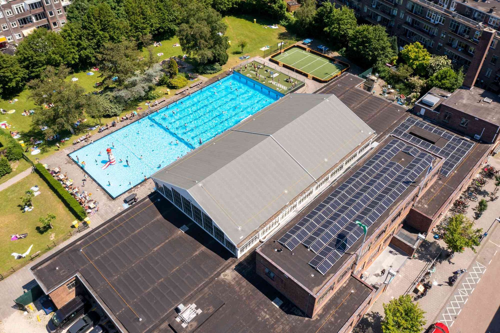 Een luchtfoto van een zwembad en een gebouw met zonnepanelen op het dak.