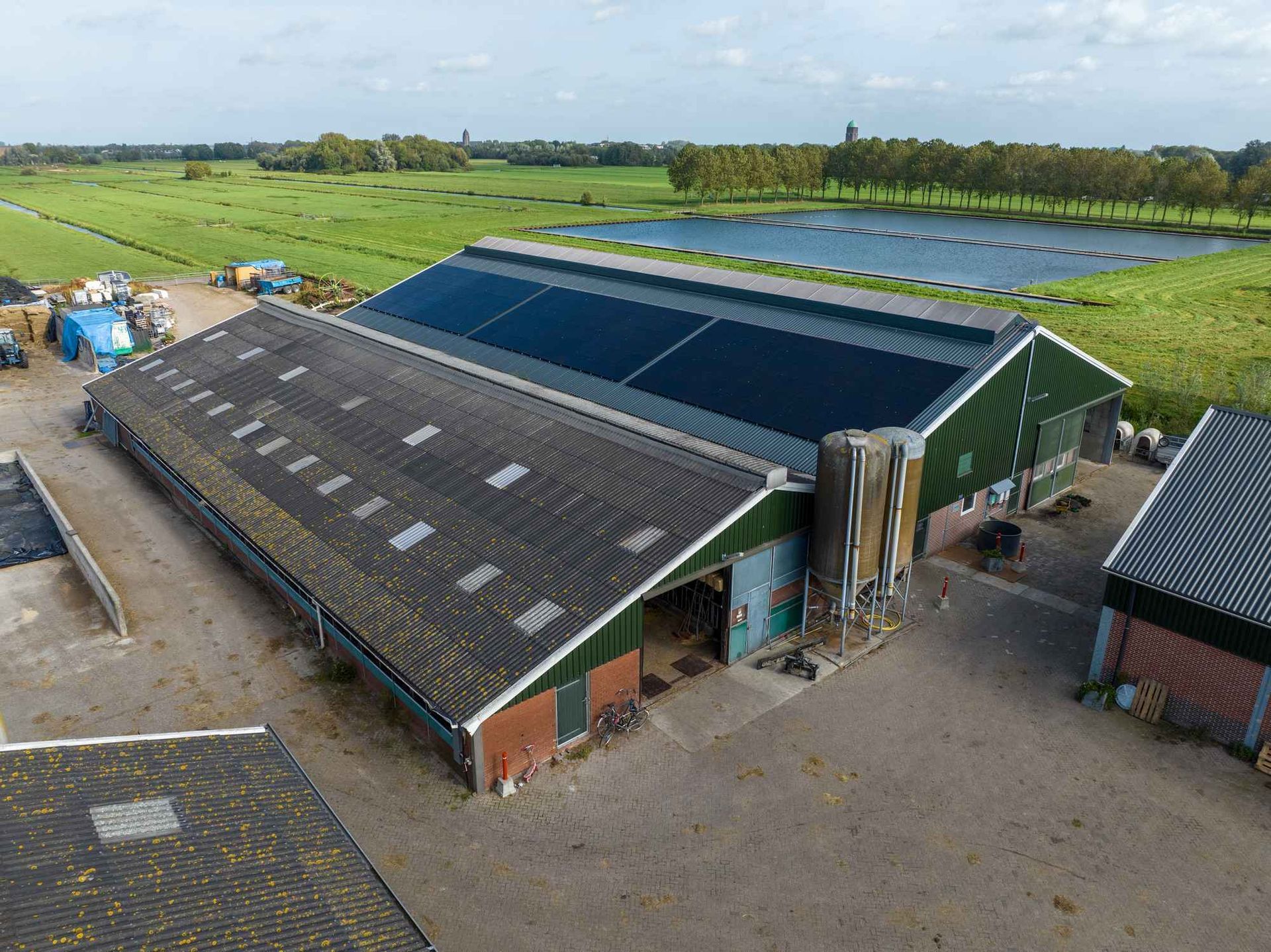 Een luchtfoto van een grote groene schuur met zonnepanelen op het dak.