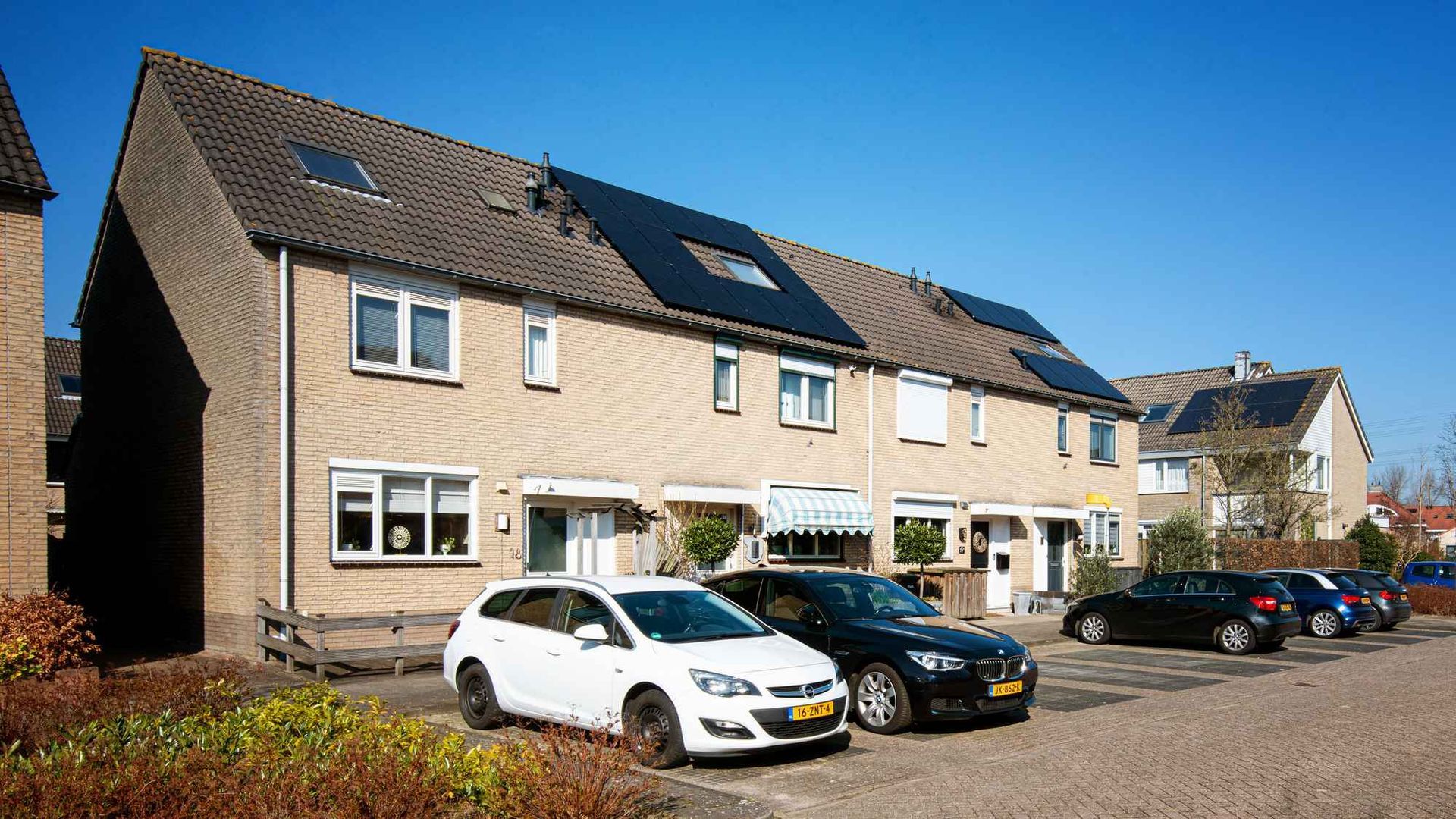 Een rij auto's staat geparkeerd voor een huis met zonnepanelen op het dak.