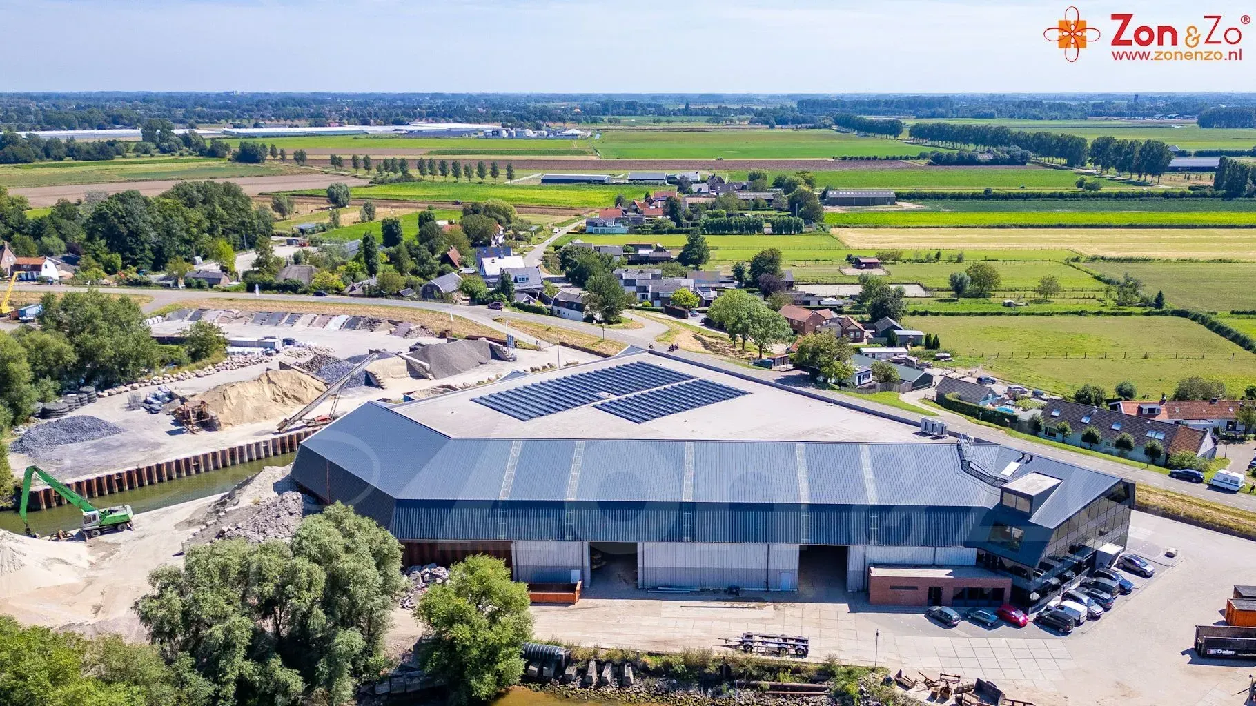 Een luchtfoto van een groot gebouw met zonnepanelen op het dak, omgeven door velden.