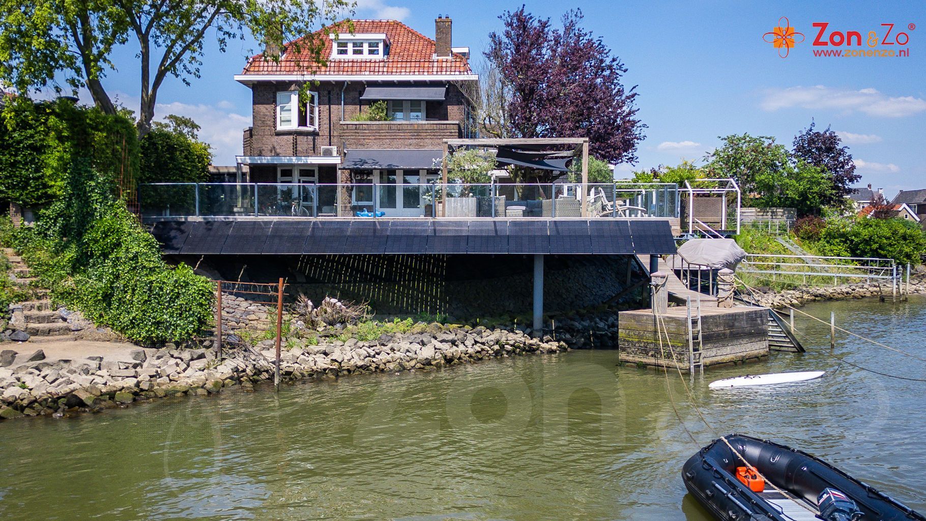 Een boot drijft voor een groot huis op een rivier.