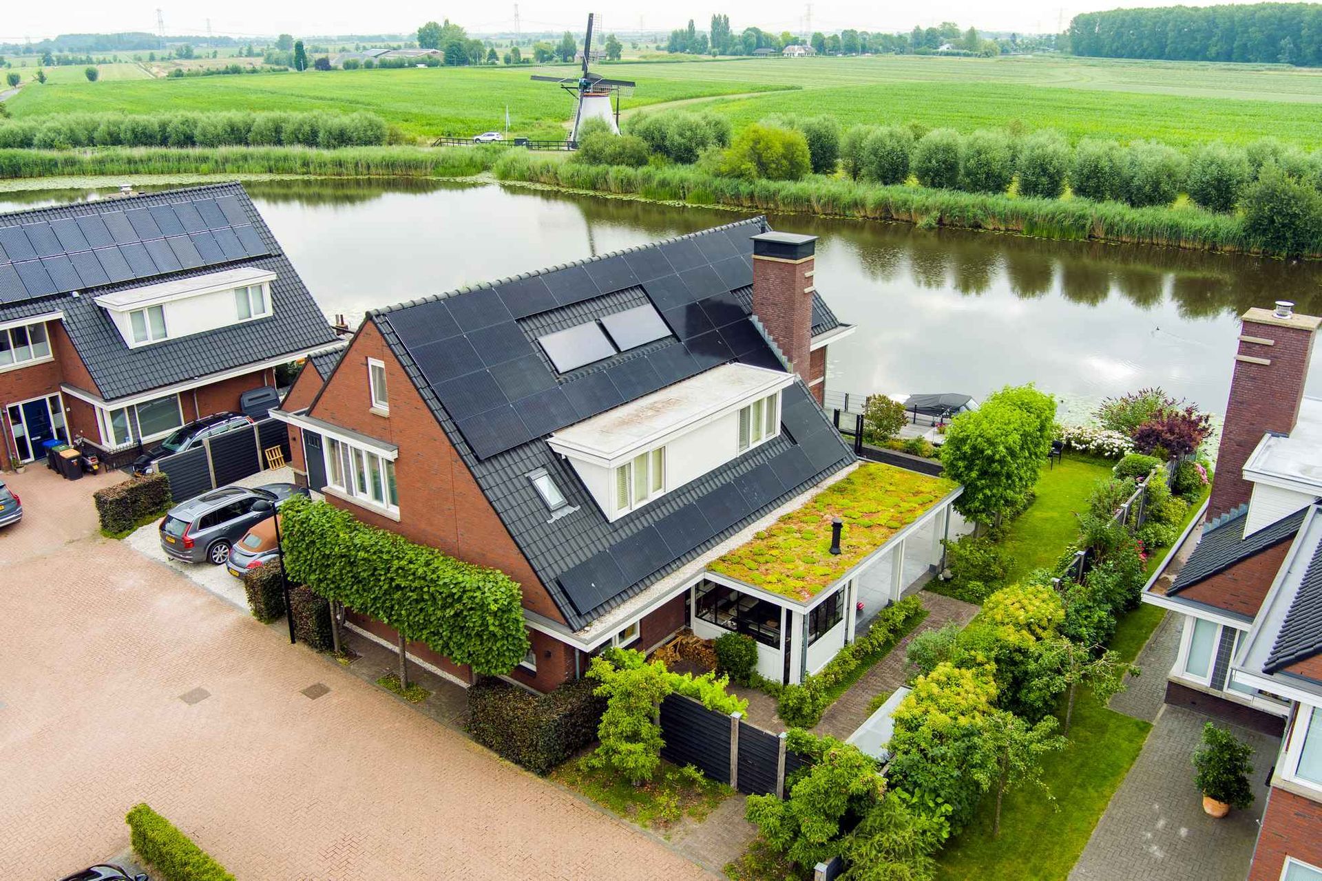 Een luchtfoto van een huis met een groen dak naast een waterpartij.