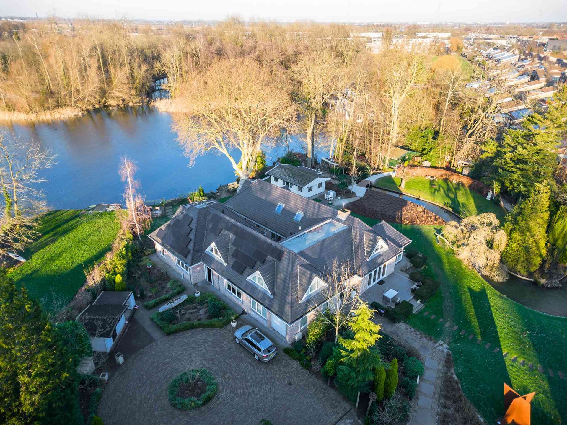 Een luchtfoto van een groot huis naast een meer, omgeven door bomen.