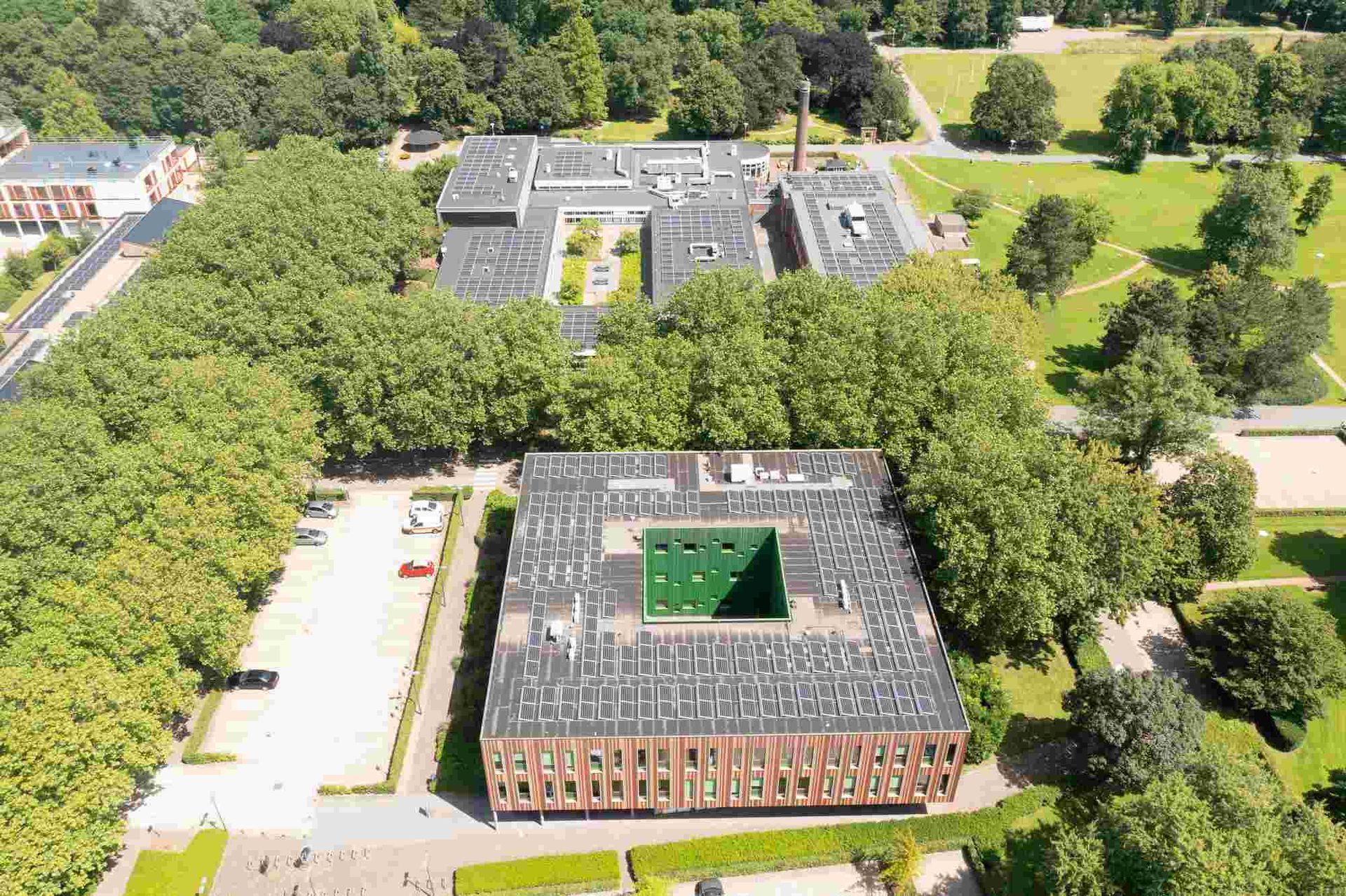 Een luchtfoto van een groot gebouw omgeven door bomen en gras.