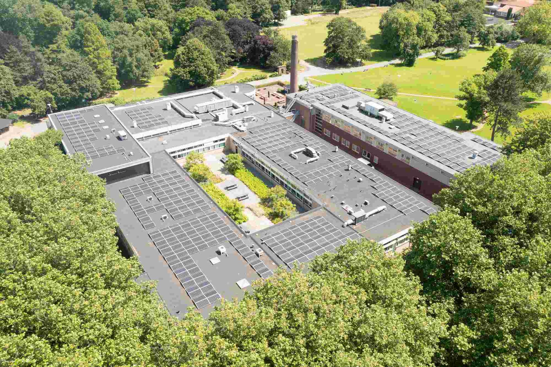 Een luchtfoto van een groot gebouw omgeven door bomen en gras.
