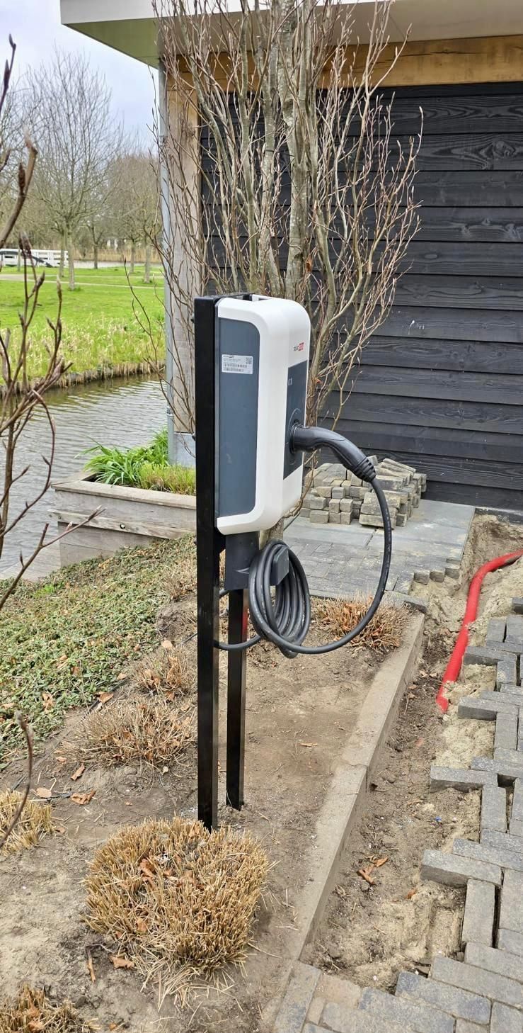 Een laadstation voor elektrische auto's staat in het zand voor een huis.