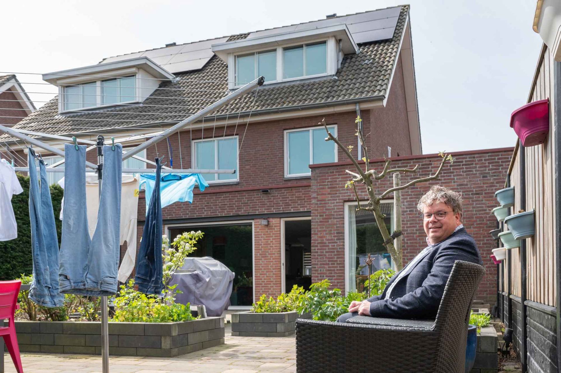 Een man zit op een stoel voor een huis.