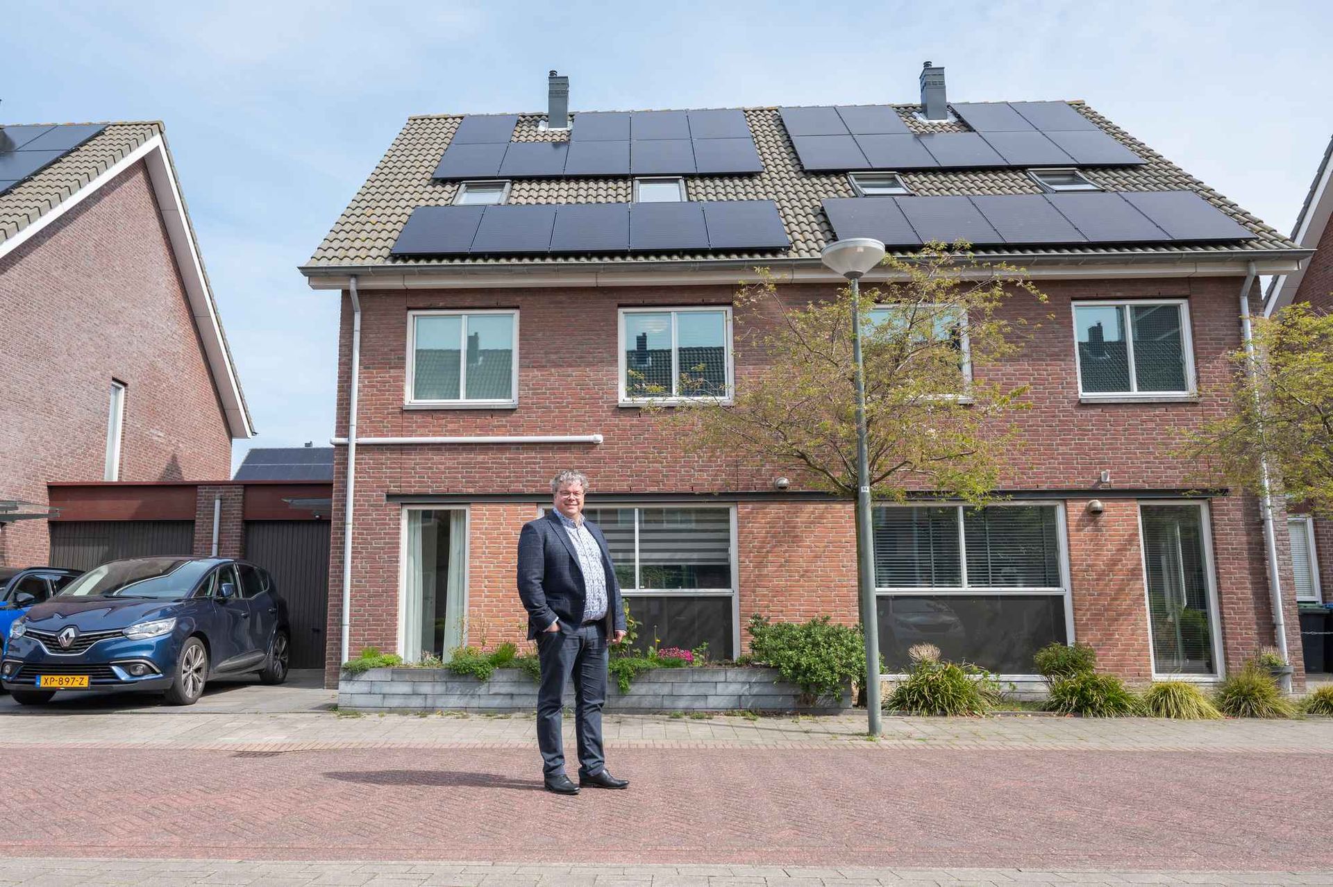 Een man staat voor een bakstenen huis met zonnepanelen op het dak.