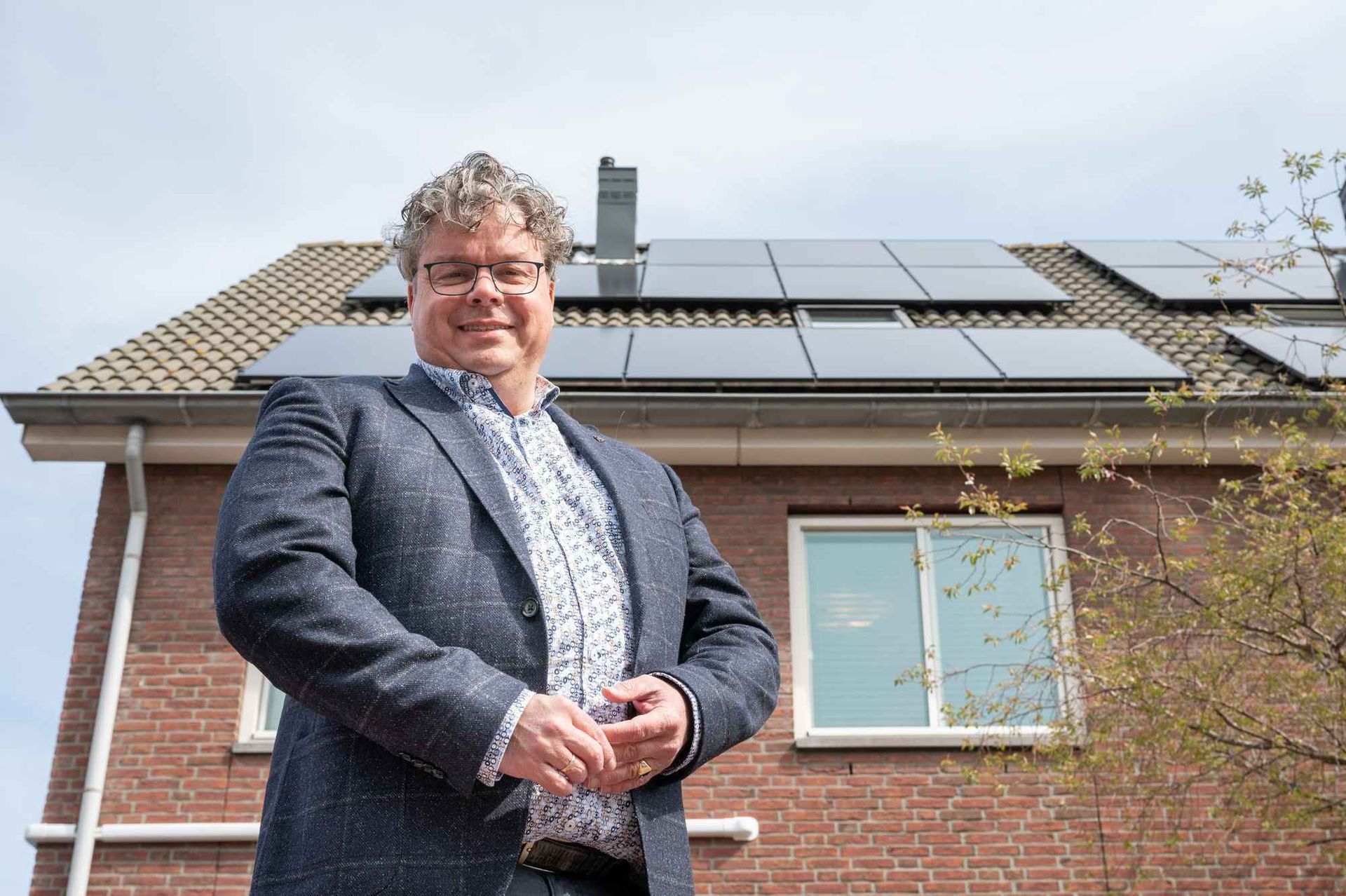 Een man in pak staat voor een huis met zonnepanelen op het dak.
