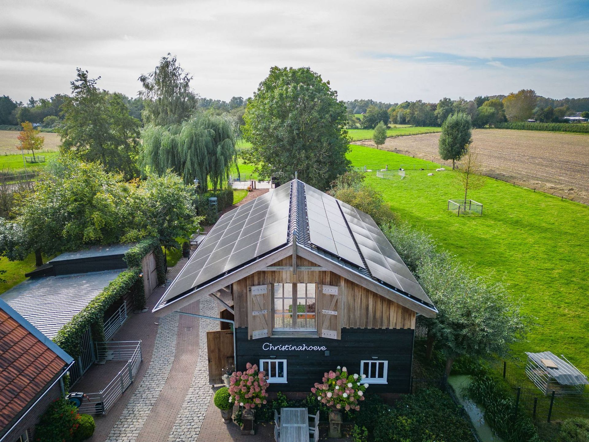 Een luchtfoto van een huis met zonnepanelen op het dak, midden in een veld.