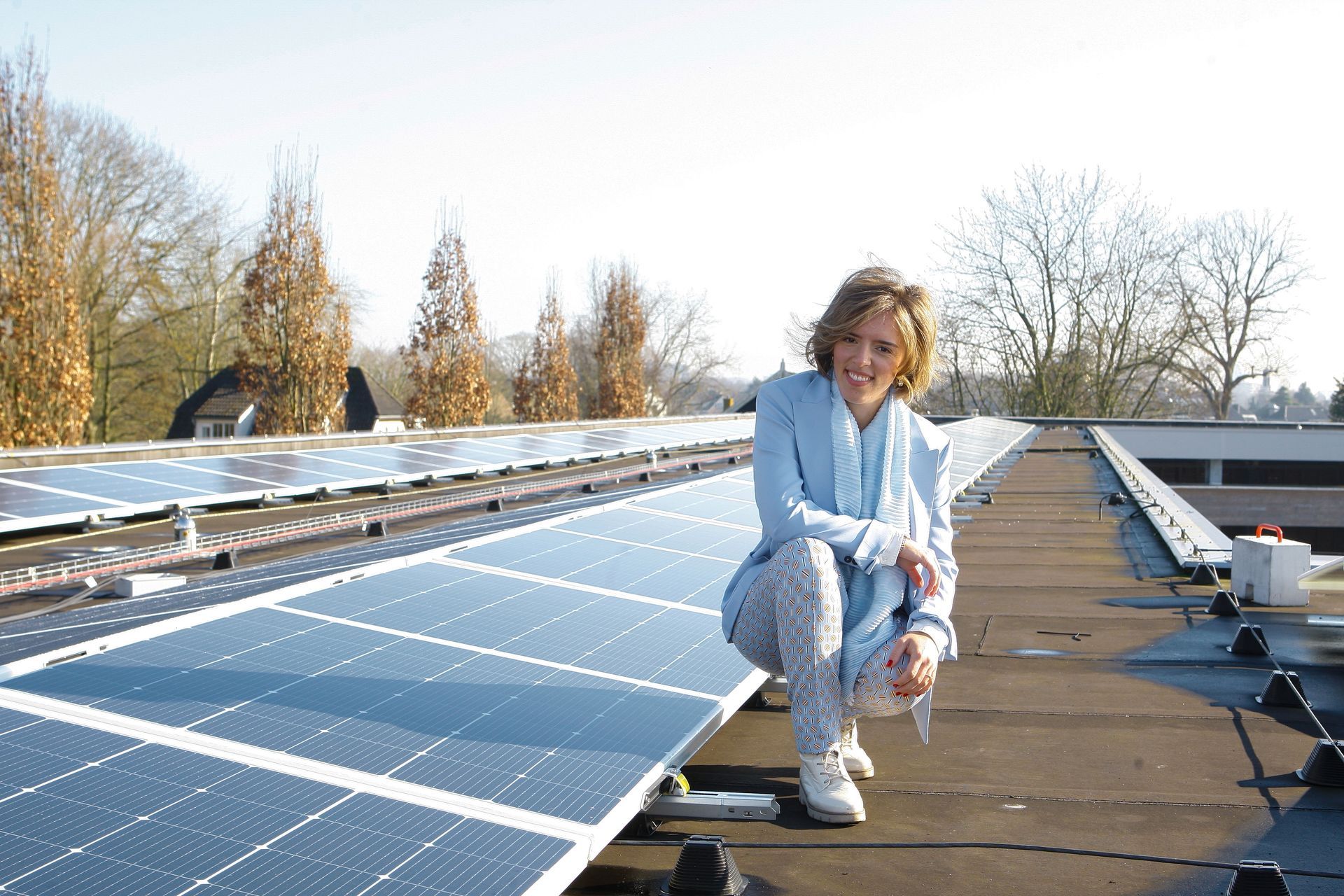 Een vrouw knielt op een dak naast een rij zonnepanelen.