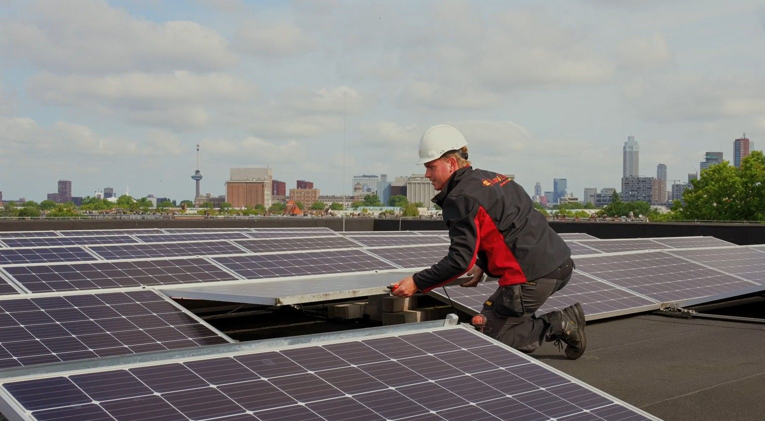 Een man installeert zonnepanelen op het dak van een gebouw.