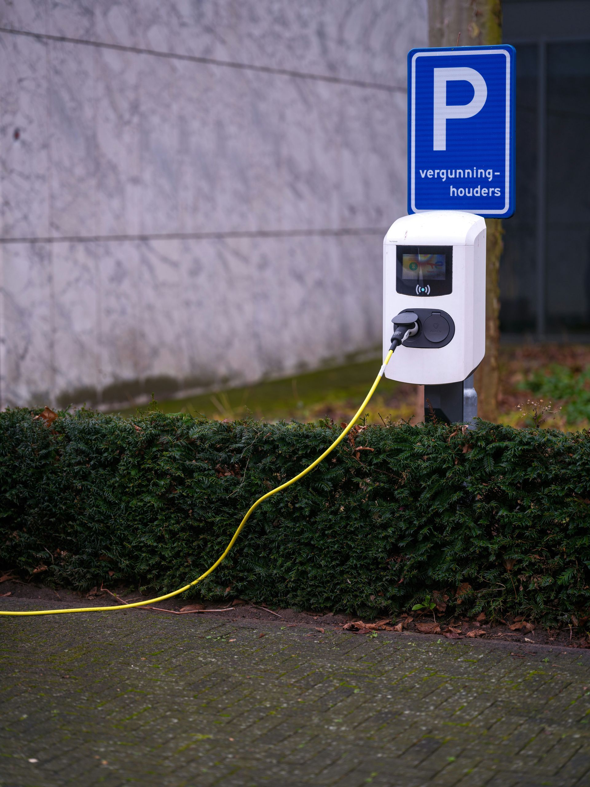 Een elektrische auto wordt opgeladen bij een laadstation voor een parkeerbord.
