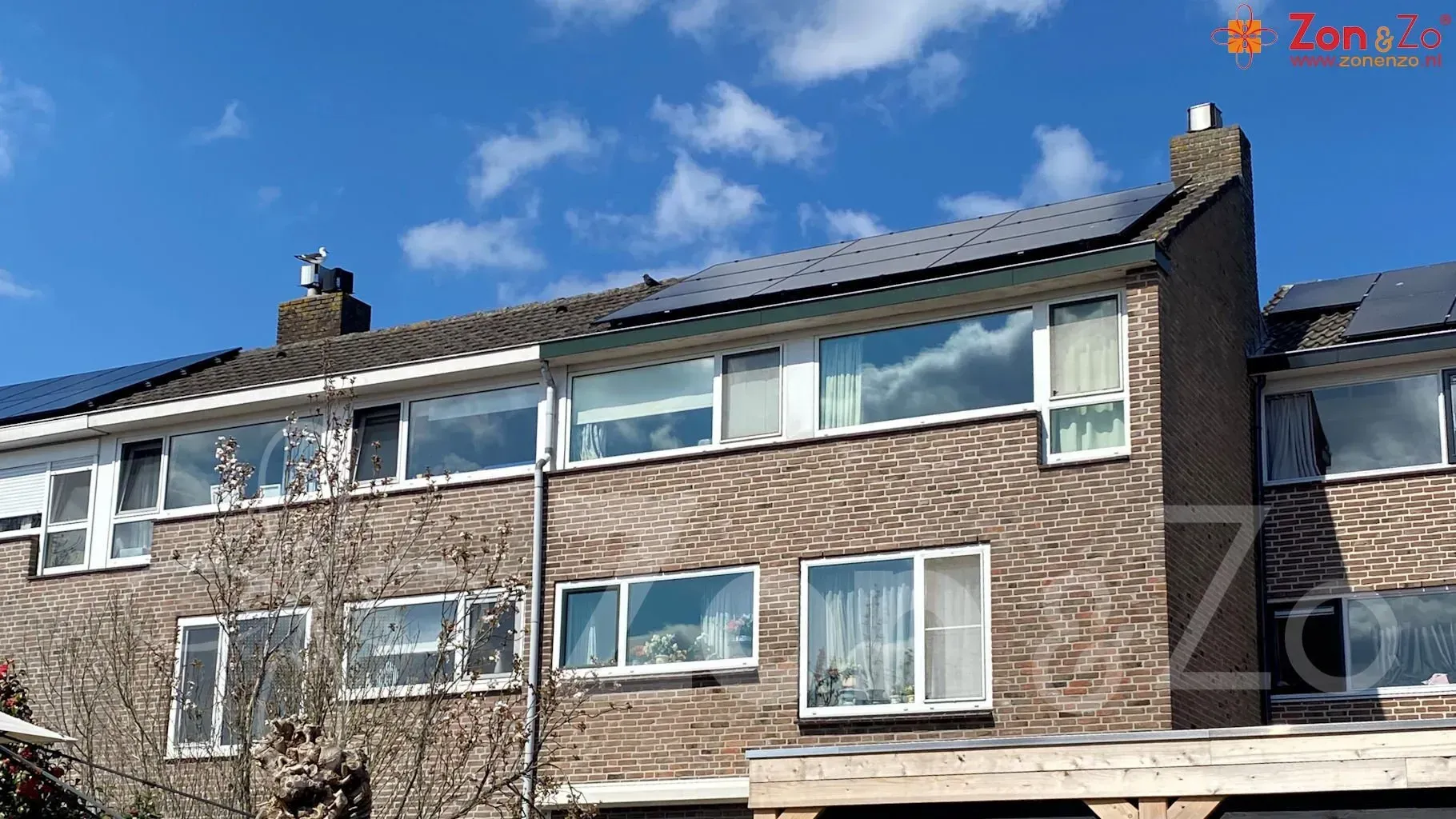 Een bakstenen huis met veel ramen en zonnepanelen op het dak