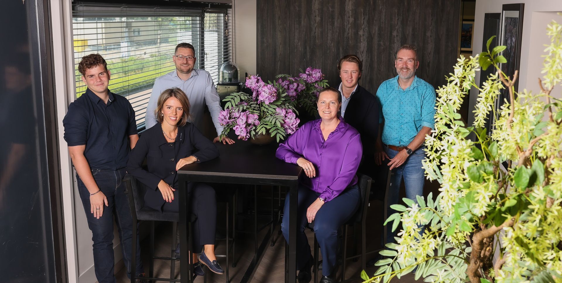 Een groep mensen poseert voor een foto voor een tafel met bloemen.