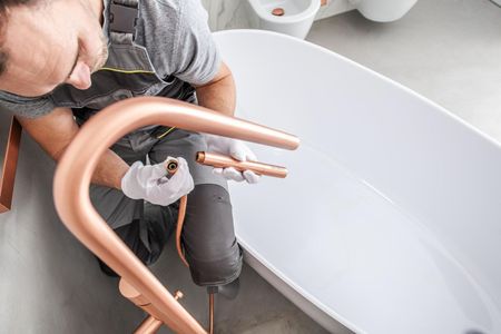 A man is fixing a bathtub faucet in a bathroom.