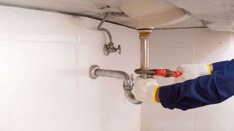 A plumber is fixing a sink pipe with a drill.