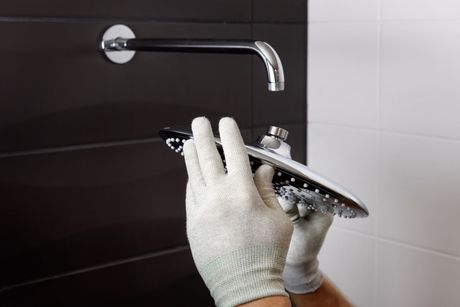 A person is fixing a shower head in a bathroom.