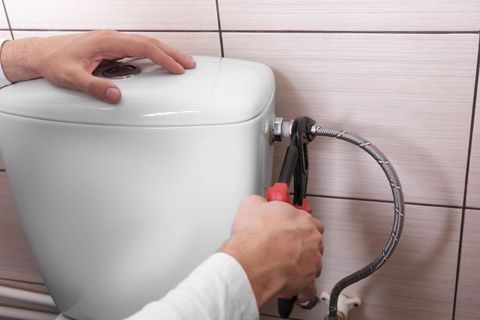 A person is fixing a toilet with a pair of pliers.