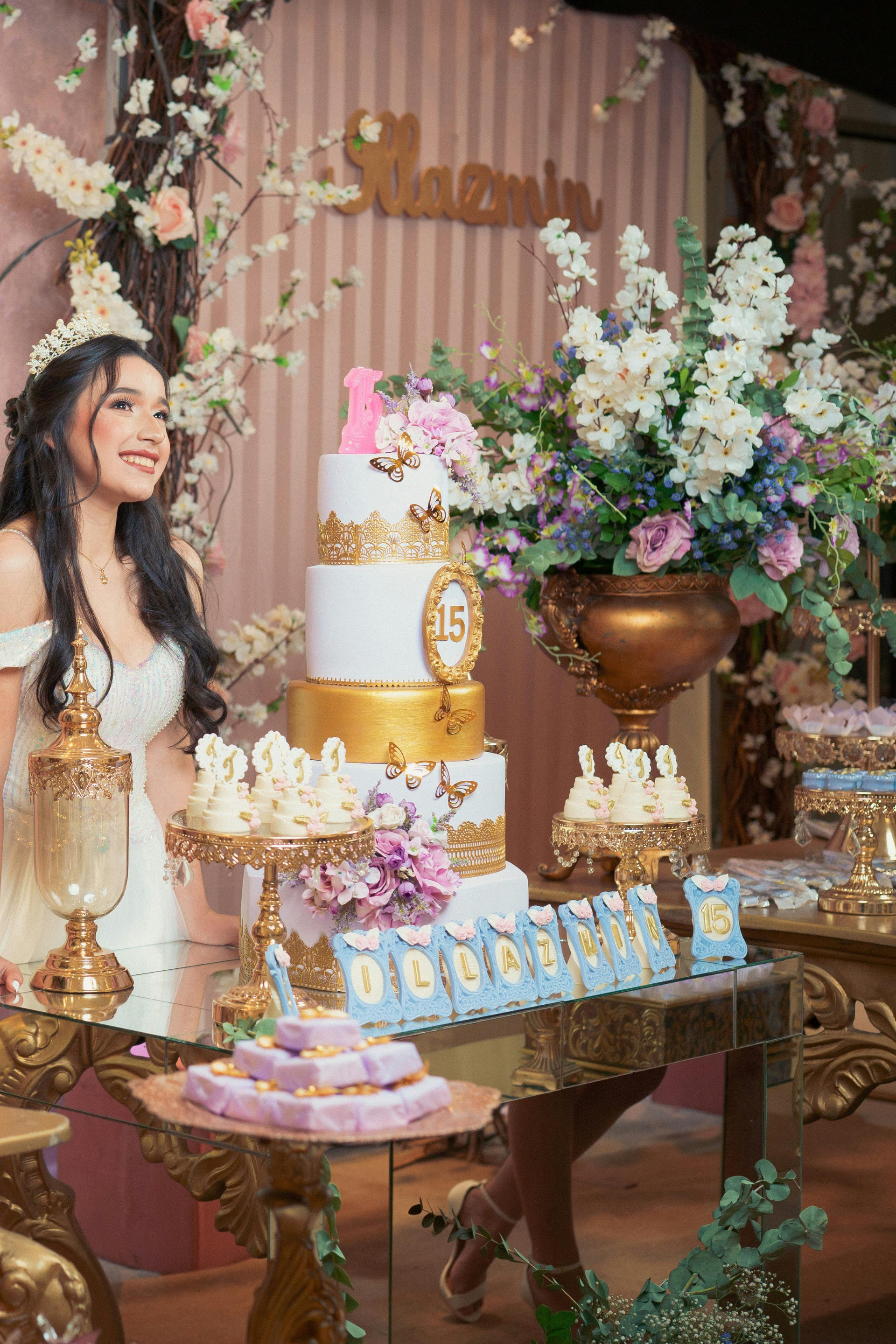 A woman is standing in front of a table with a cake and flowers.