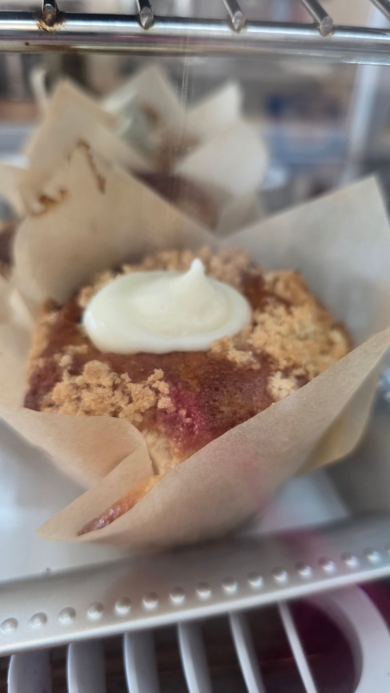 A chocolate chip cookie is sitting on a wooden cutting board in a glass case.