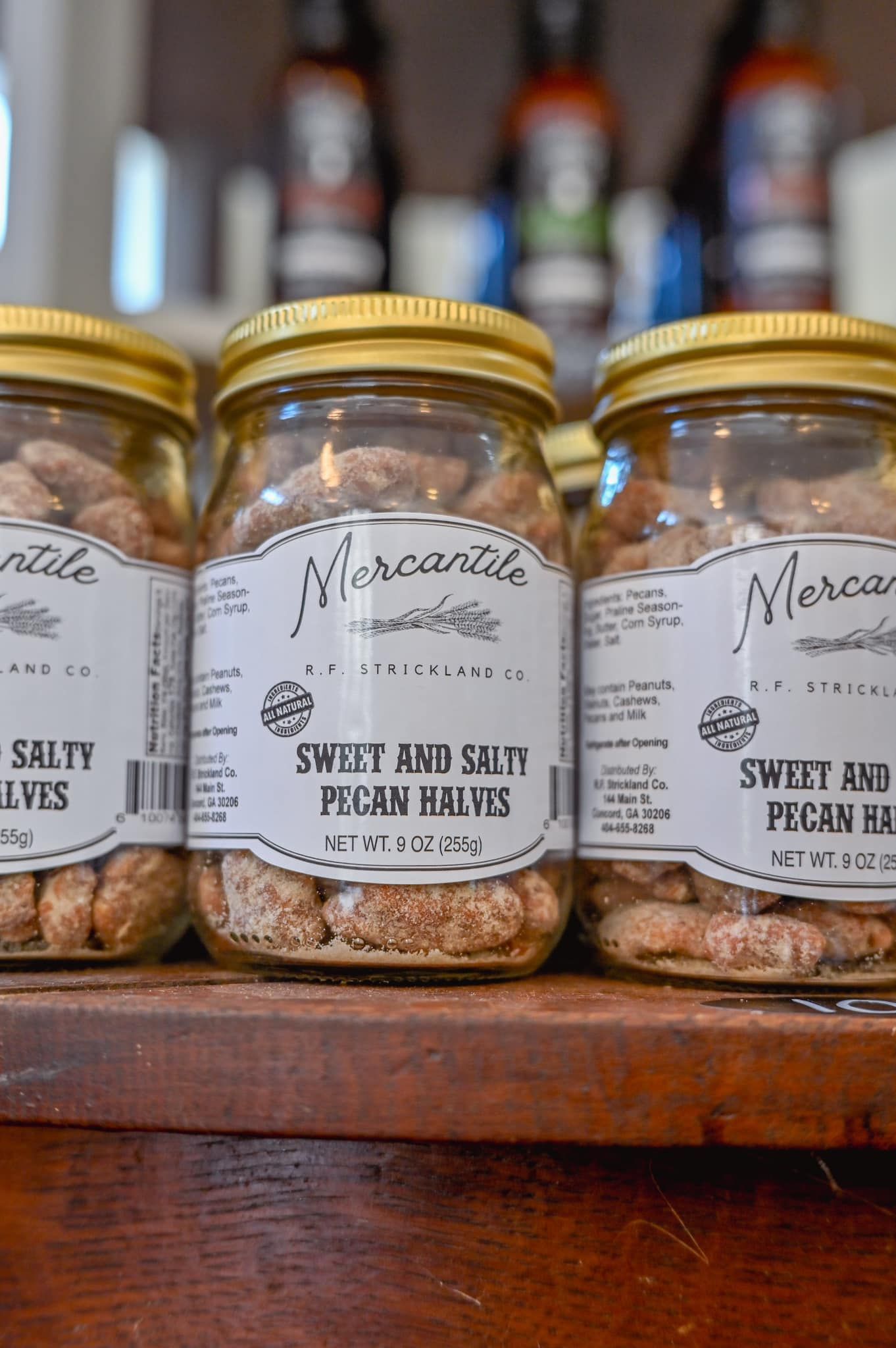 Three jars of pecans are sitting on a wooden shelf.