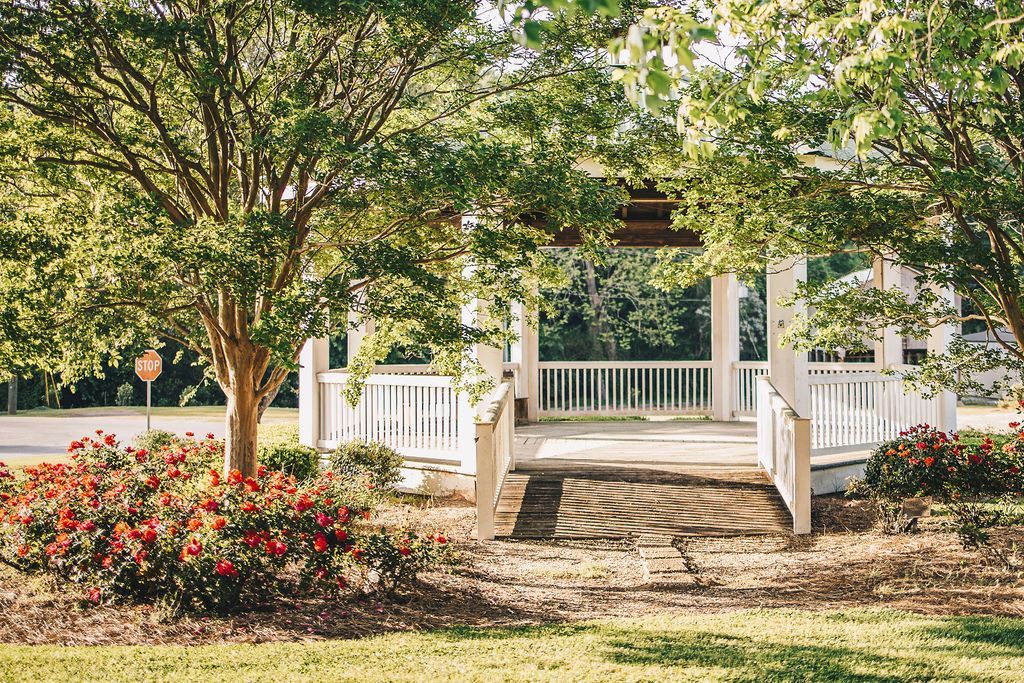 A gazebo is surrounded by trees and flowers in a park.