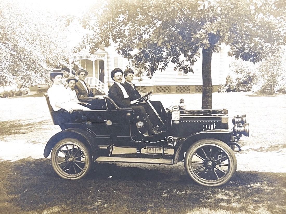 A black and white photo of a group of people in an old car
