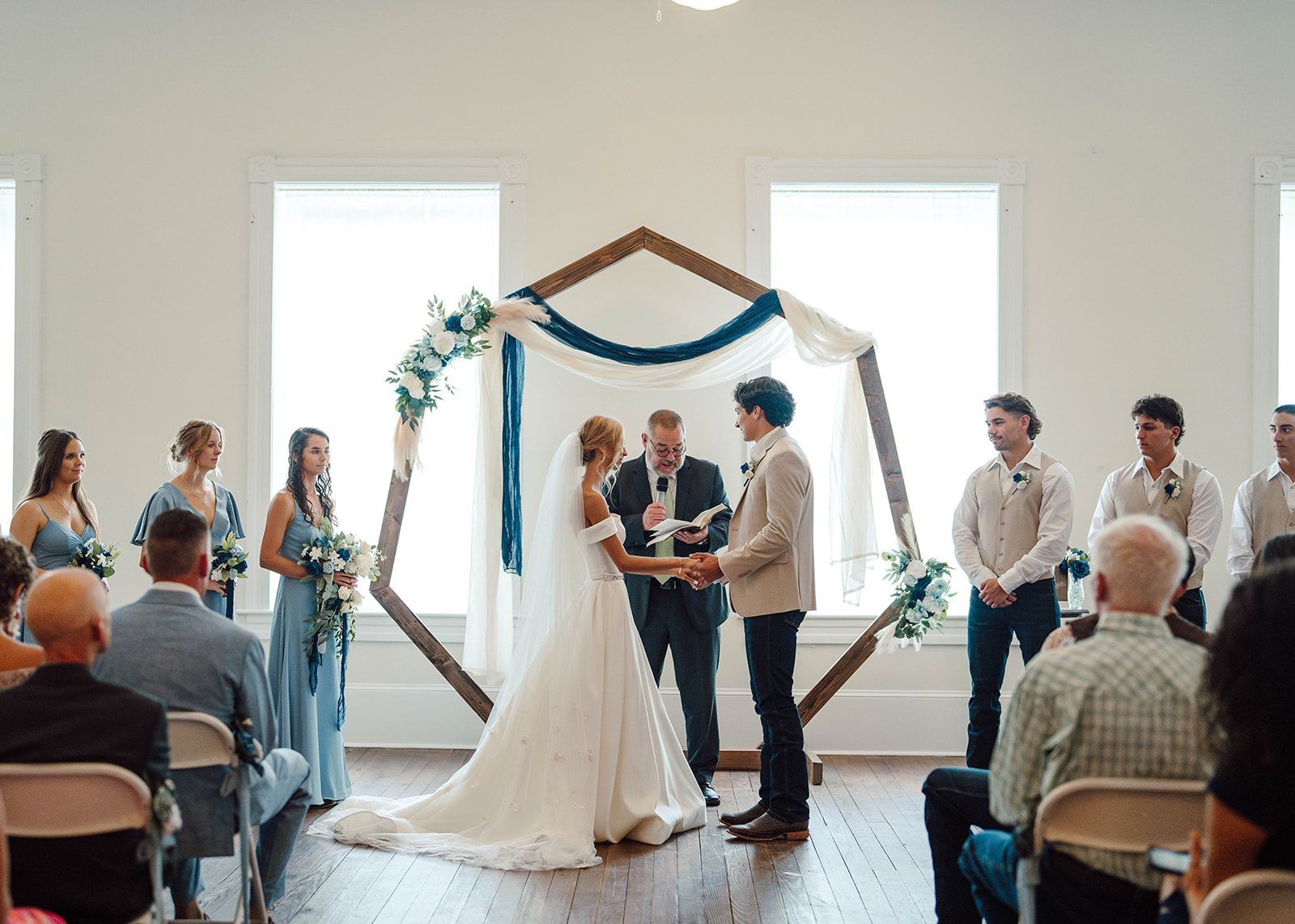 A bride and groom are standing under a floral arch in the desert.