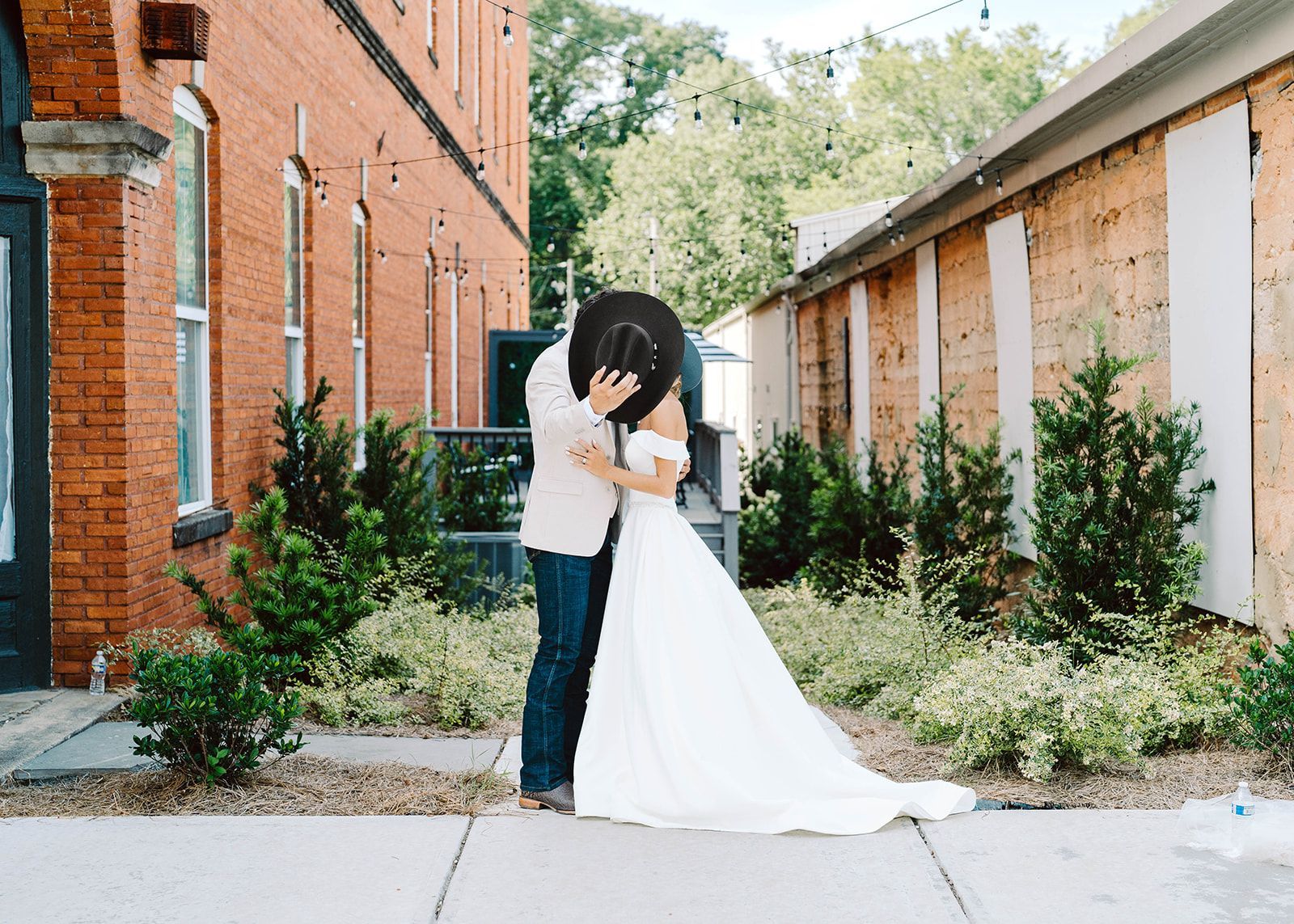 A bride and groom are kissing on the sidewalk in front of a brick building.