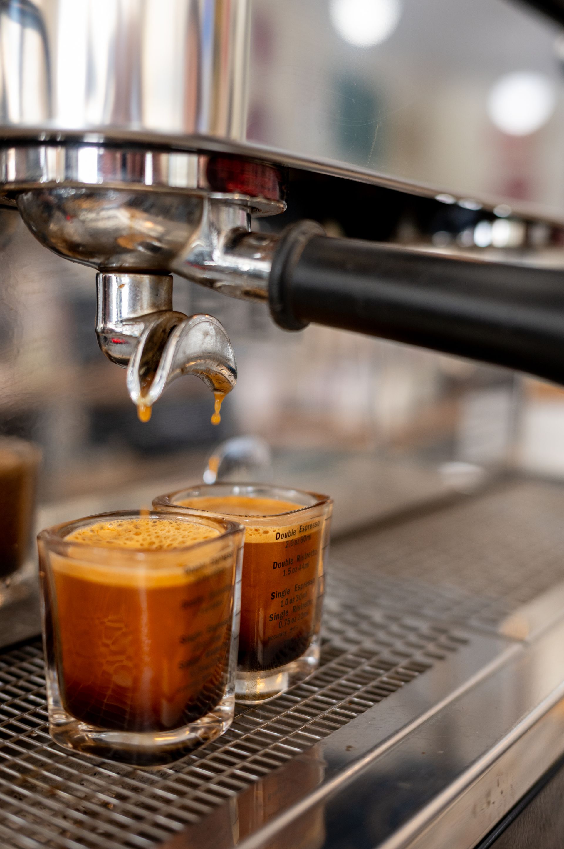 Three shot glasses of espresso are being poured from a coffee machine.