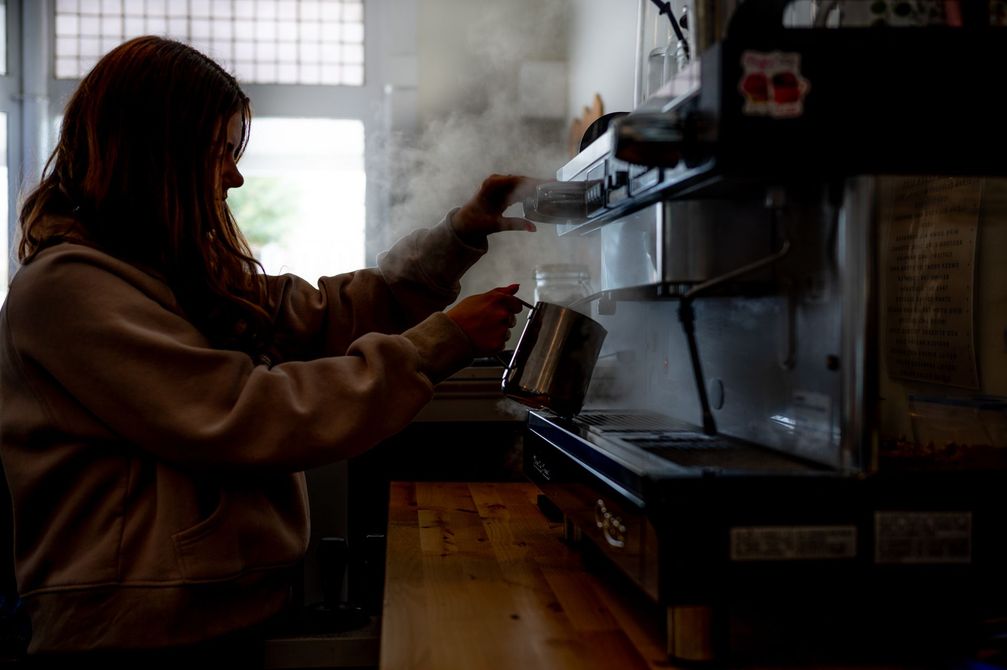 A woman is pouring coffee into a cup in a kitchen.