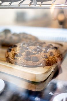 A chocolate chip cookie is sitting on a wooden cutting board in a glass case.