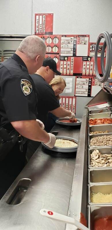 A group of police officers are preparing pizzas in a kitchen.