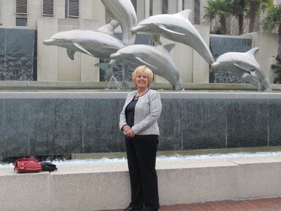 A woman is standing in front of a fountain with dolphins in it
