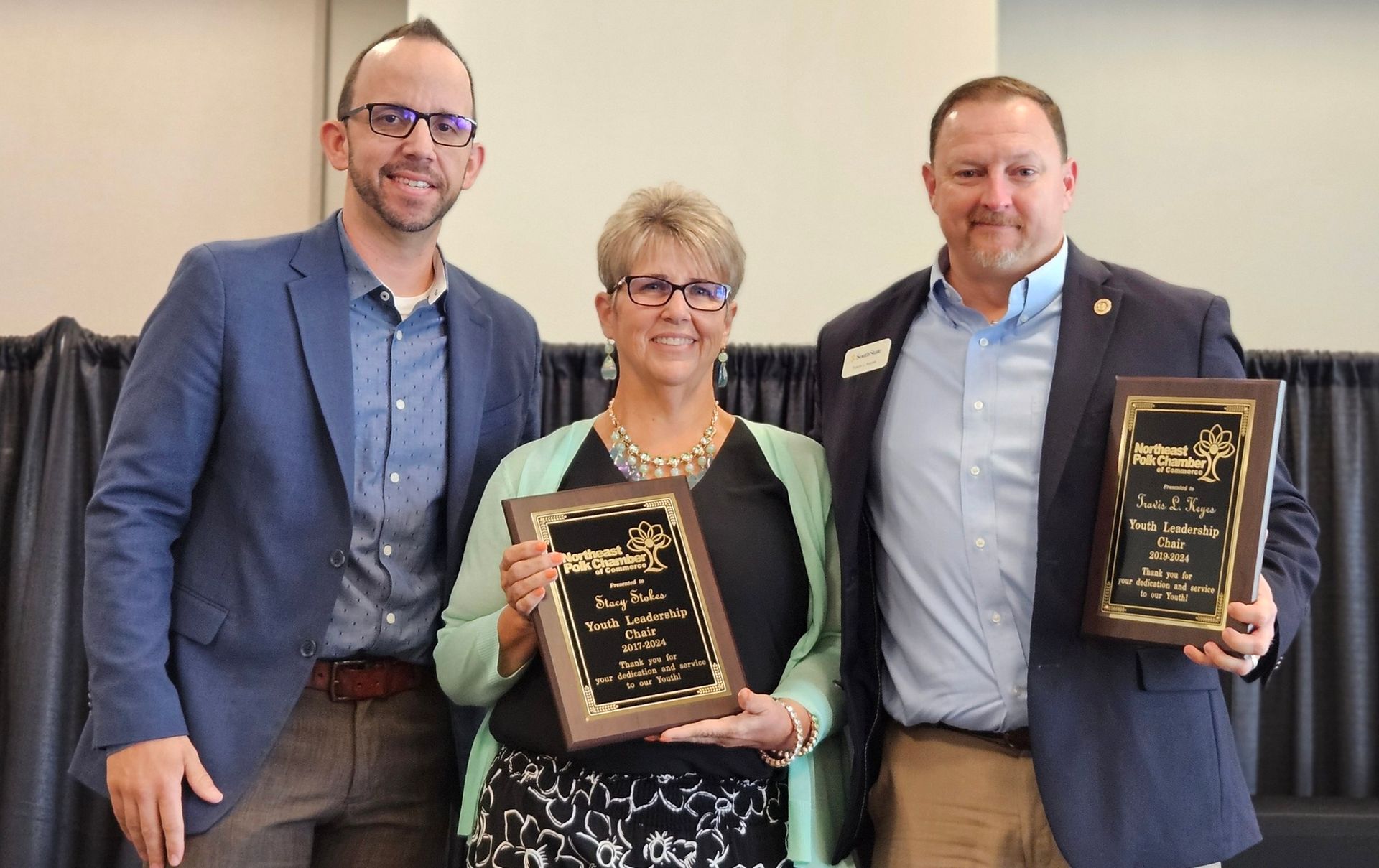 Three people are standing next to each other holding plaques.