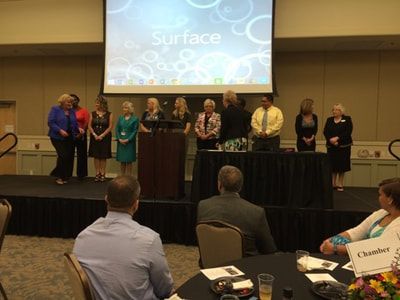 A group of people standing in front of a screen that says surface