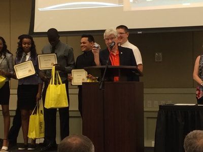 A group of people standing around a podium holding yellow bags and certificates