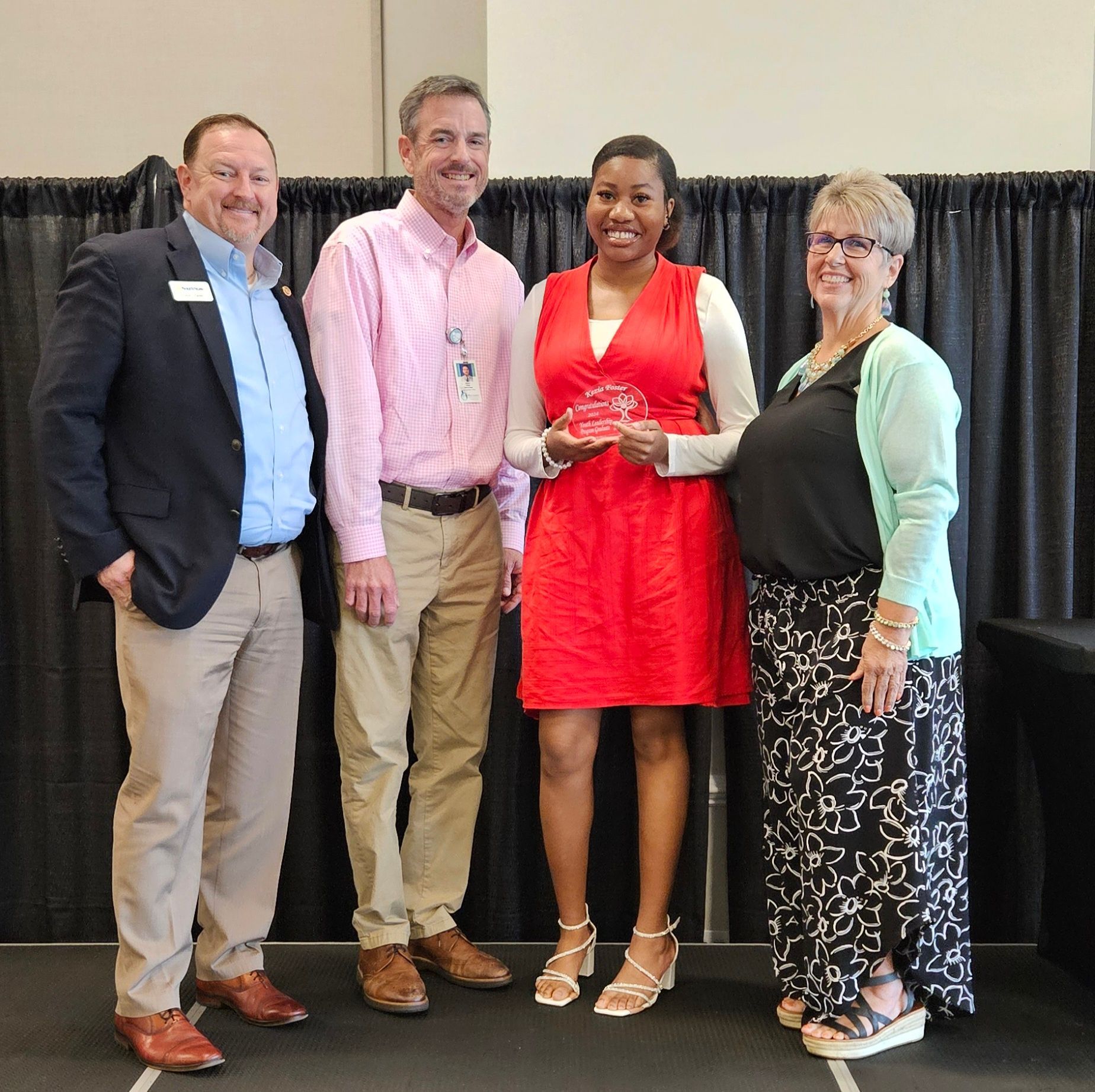 A group of people posing for a picture with a woman in a red dress holding an award