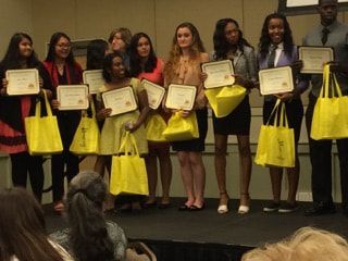A group of people are standing on a stage holding certificates and bags.
