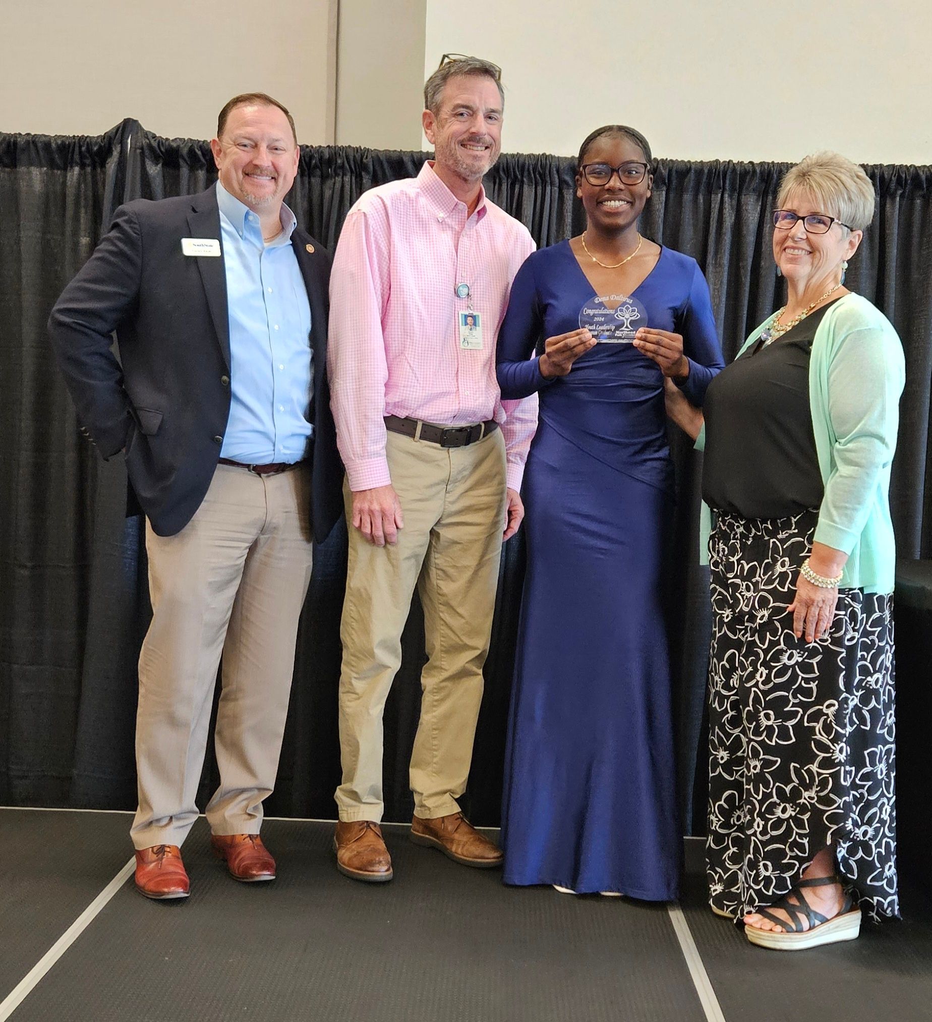 A group of people posing for a picture with one woman holding an award