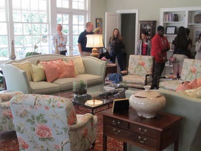 A group of people are standing around a living room filled with furniture.