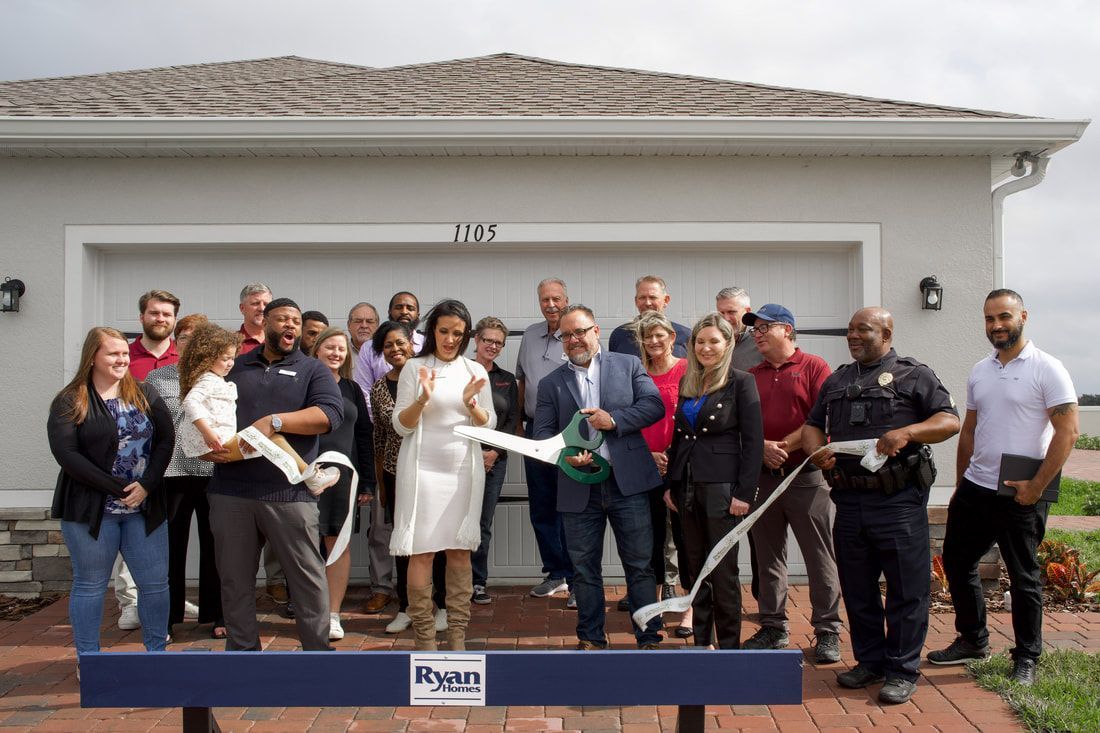 A group of people are standing in front of a house cutting a ribbon.