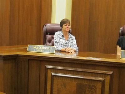 A woman is sitting at a wooden desk in a courtroom.