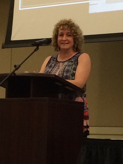 A woman stands at a podium in front of a large screen
