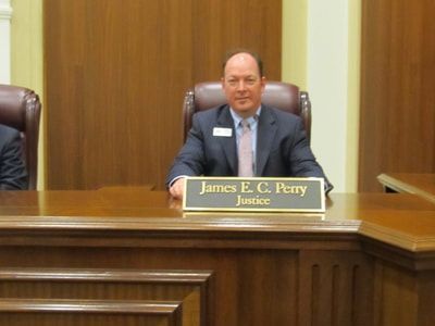 A man in a suit and tie is sitting at a judge 's bench.