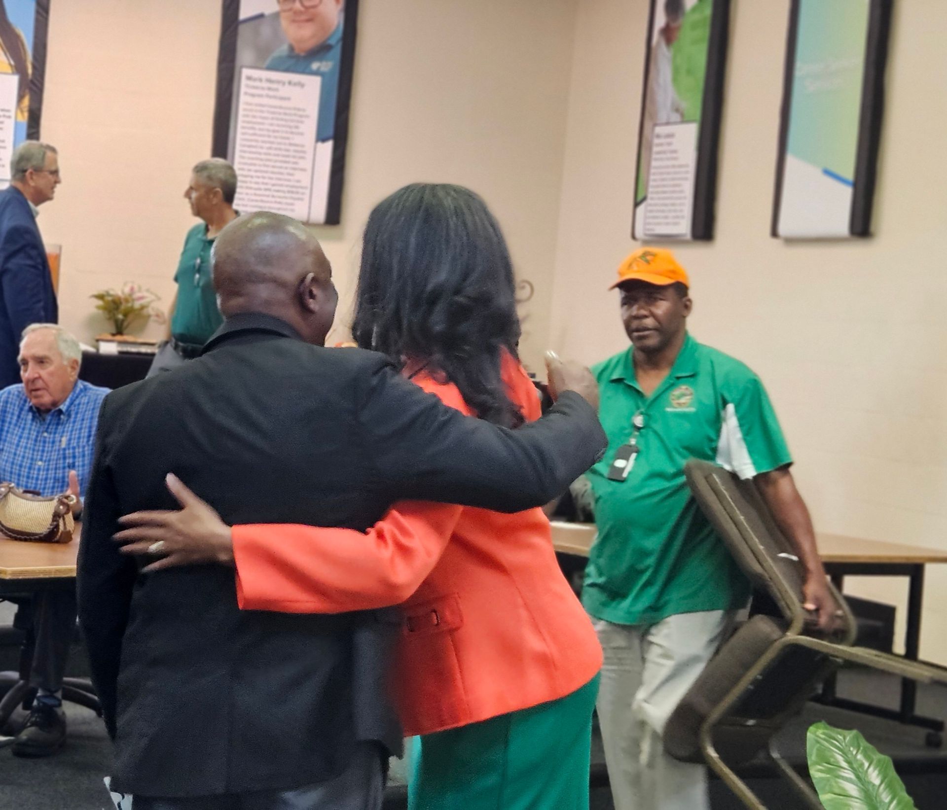 A woman in an orange jacket is hugging a man in a green shirt